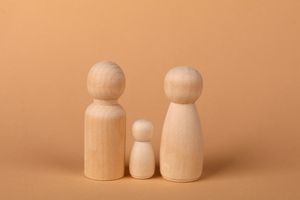 Three wooden figurines representing a family set against a warm brown backdrop.